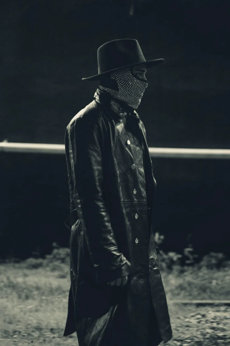 A figure in a black hat, a diamond mask and a long leather coat.