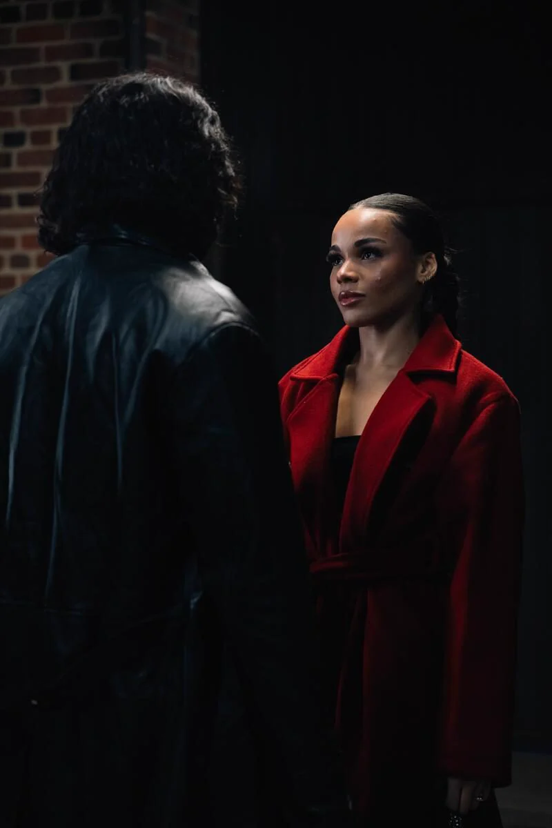 A woman in a red coat faces a man in a black leather coat.